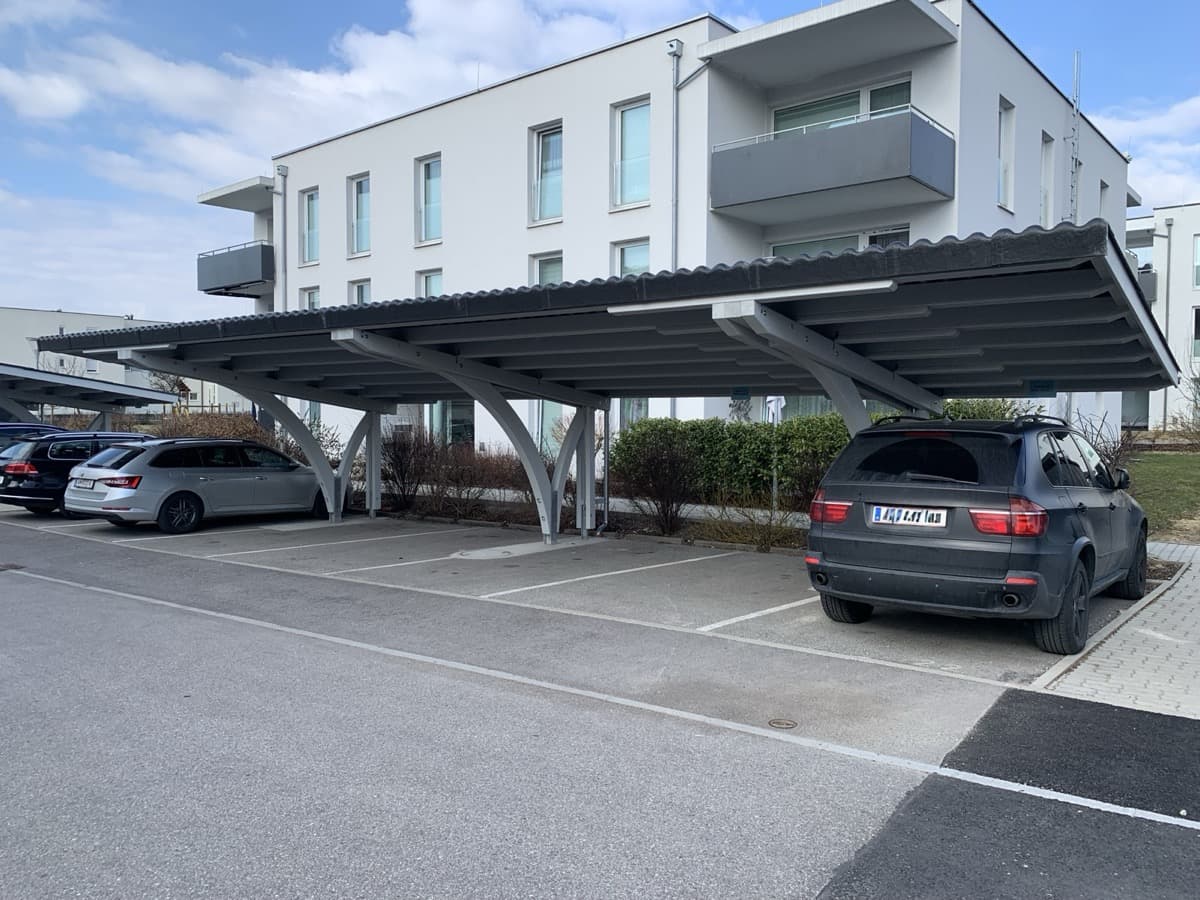 Moderner Stahl-Carport mit Bogenstützen bei Mehrfamilienhaus