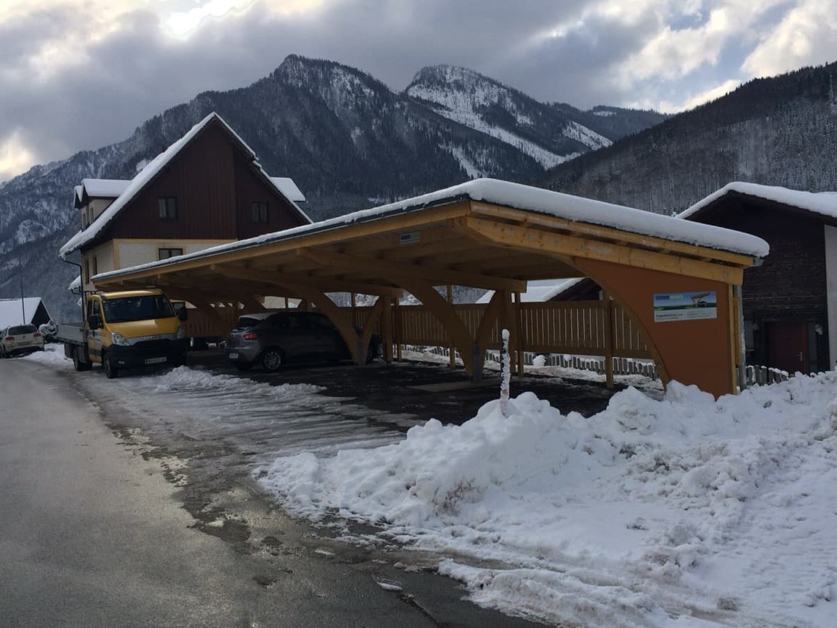 Mehrfachcarport mit Holzbogen und orangefarbener Rückwand im Winter