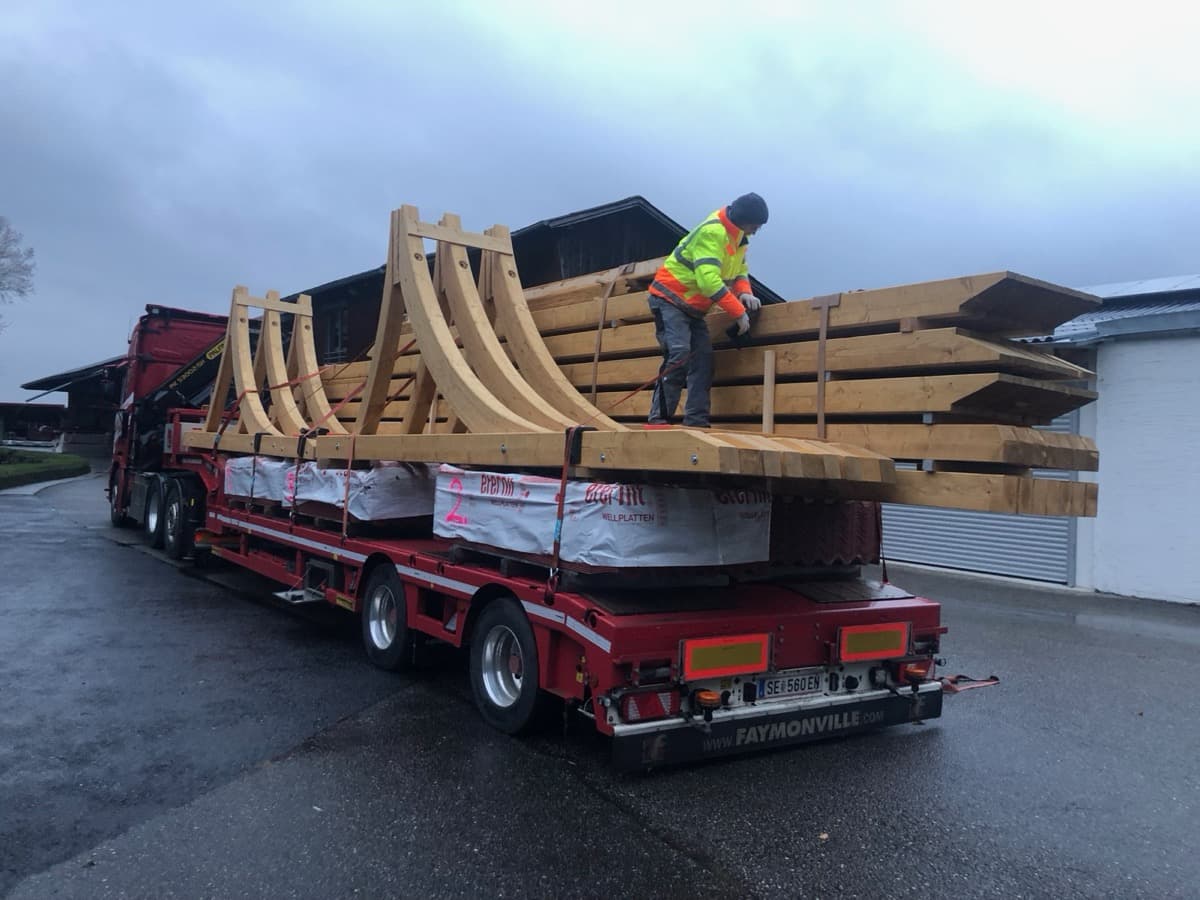 Arbeiter sichert Holzbauteile auf Tieflader-Anhänger